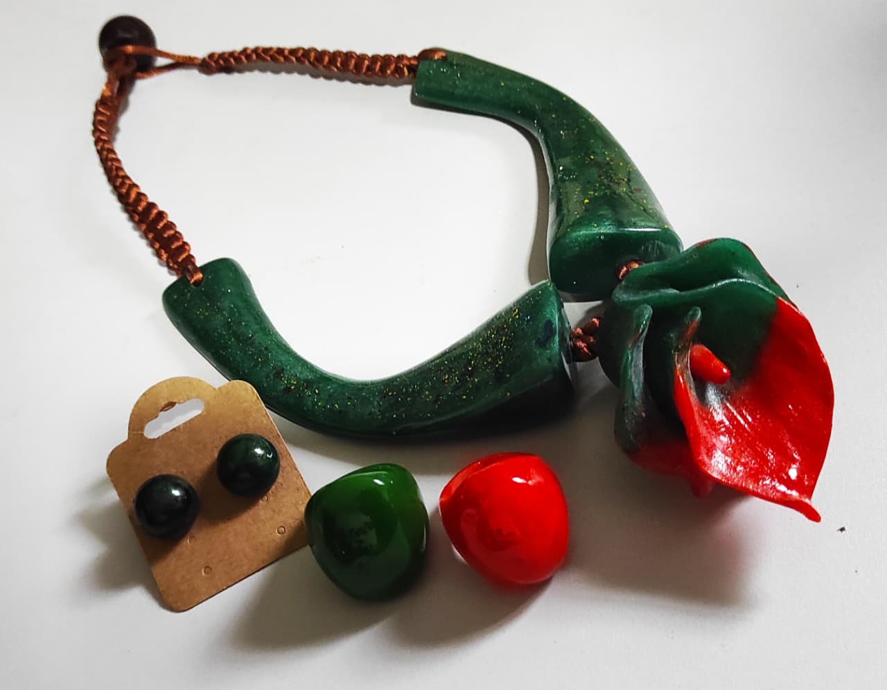 Conjunto verde com colar de copo-de-leite vermelho, brincos e anel sobre fundo claro