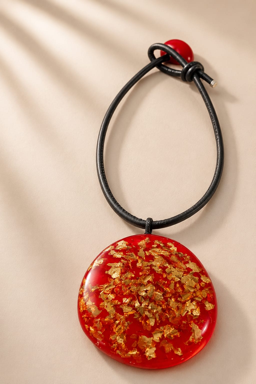 Maxi Colar Ouro: pingente circular de resina vermelha com folhas douradas e cordão preto